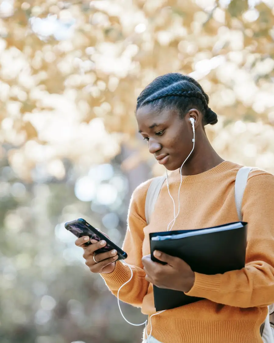 A young woman holding a folder and reading on her phone outdoors