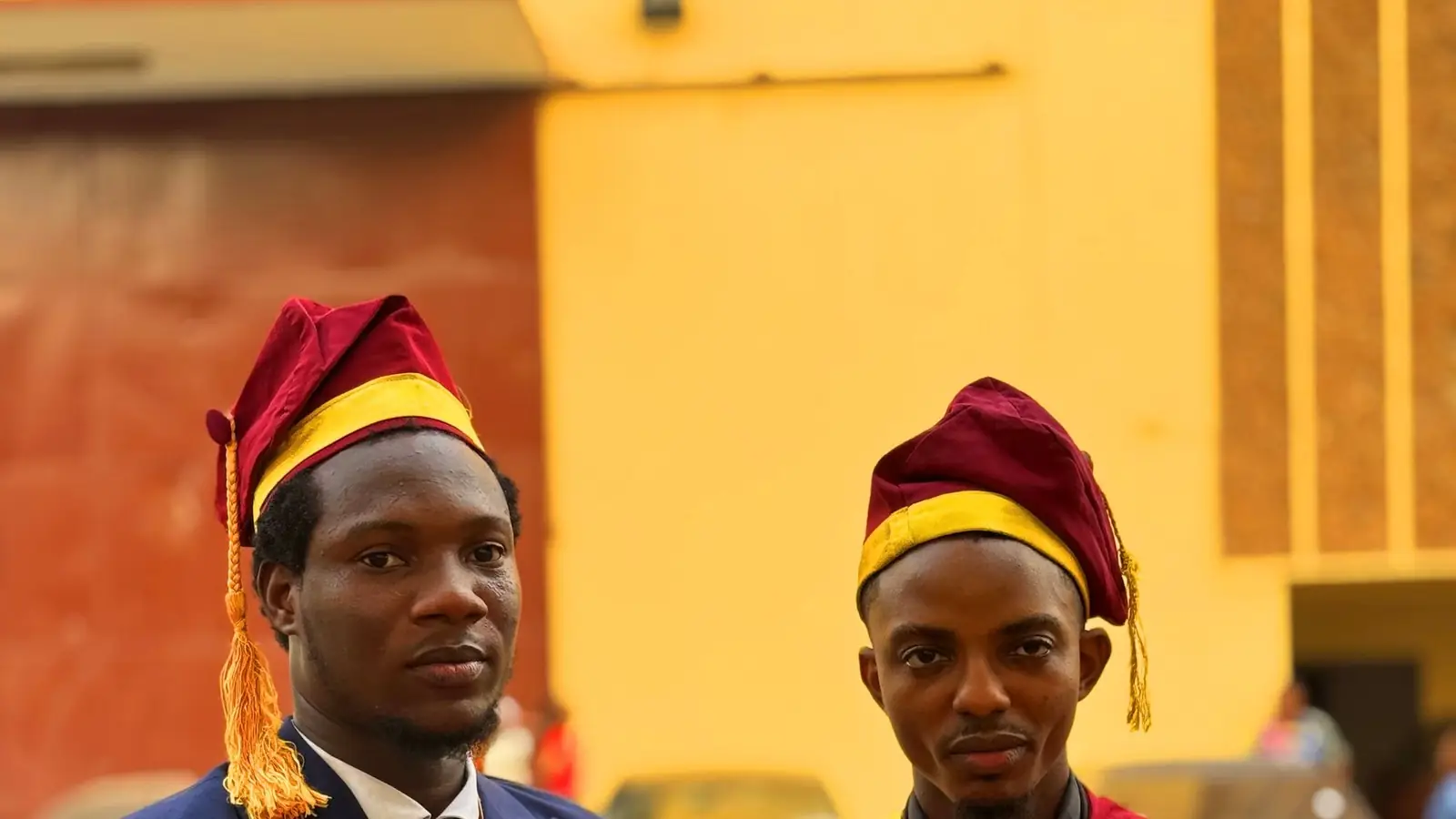 Two graduates in maroon and gold gowns standing together