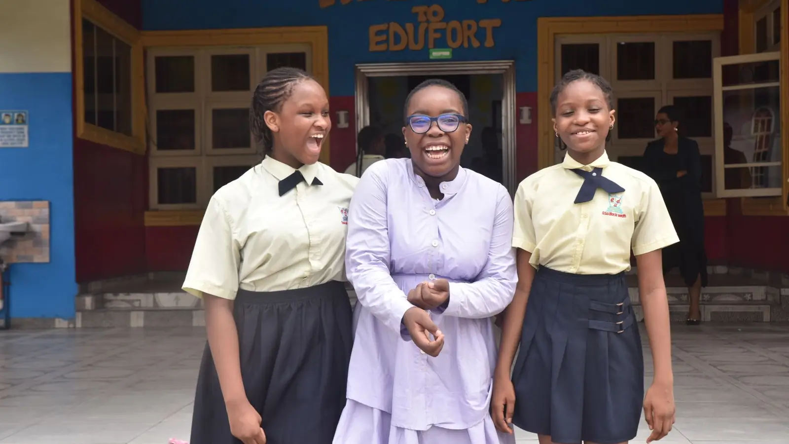 Three secondary-school students in uniform standing outside their school