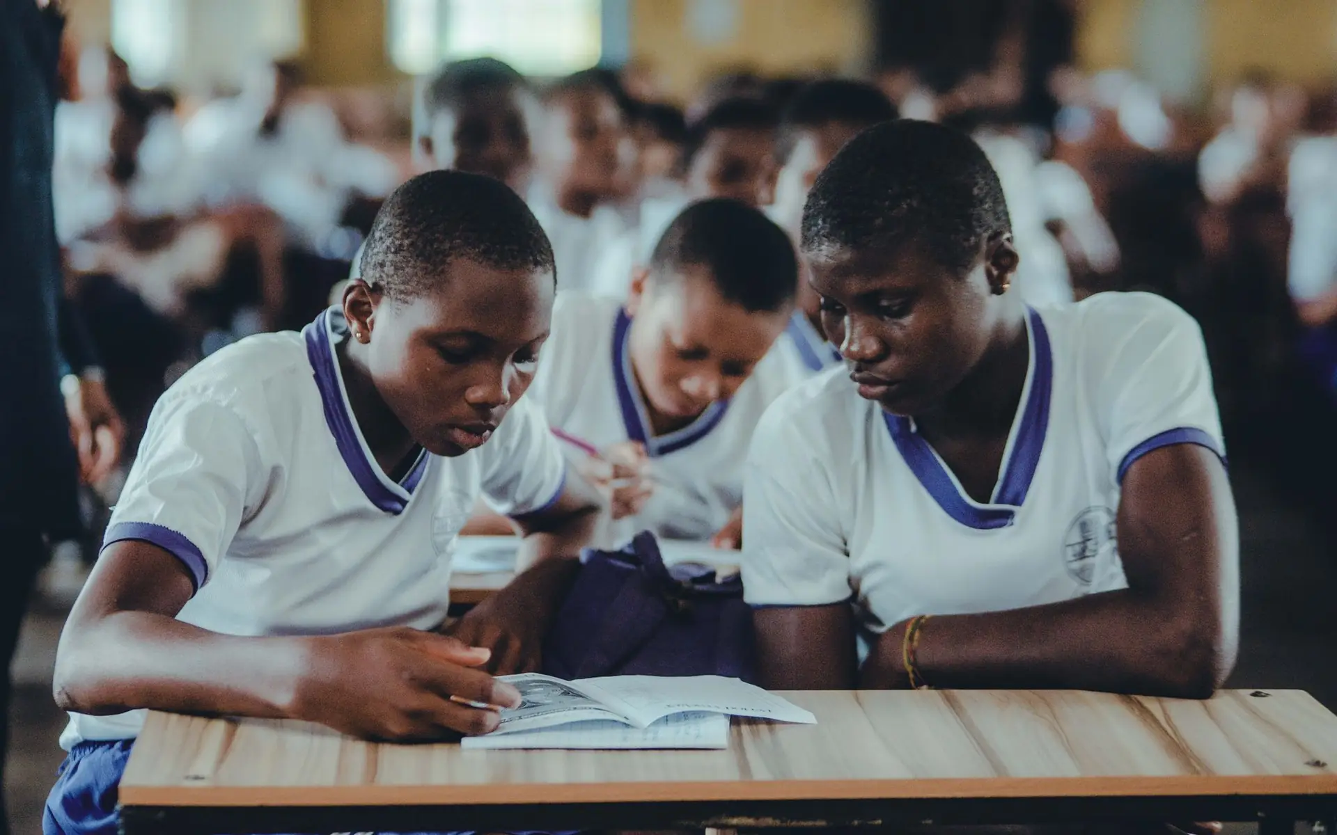 Secondary-school students in white uniforms working together at their desks