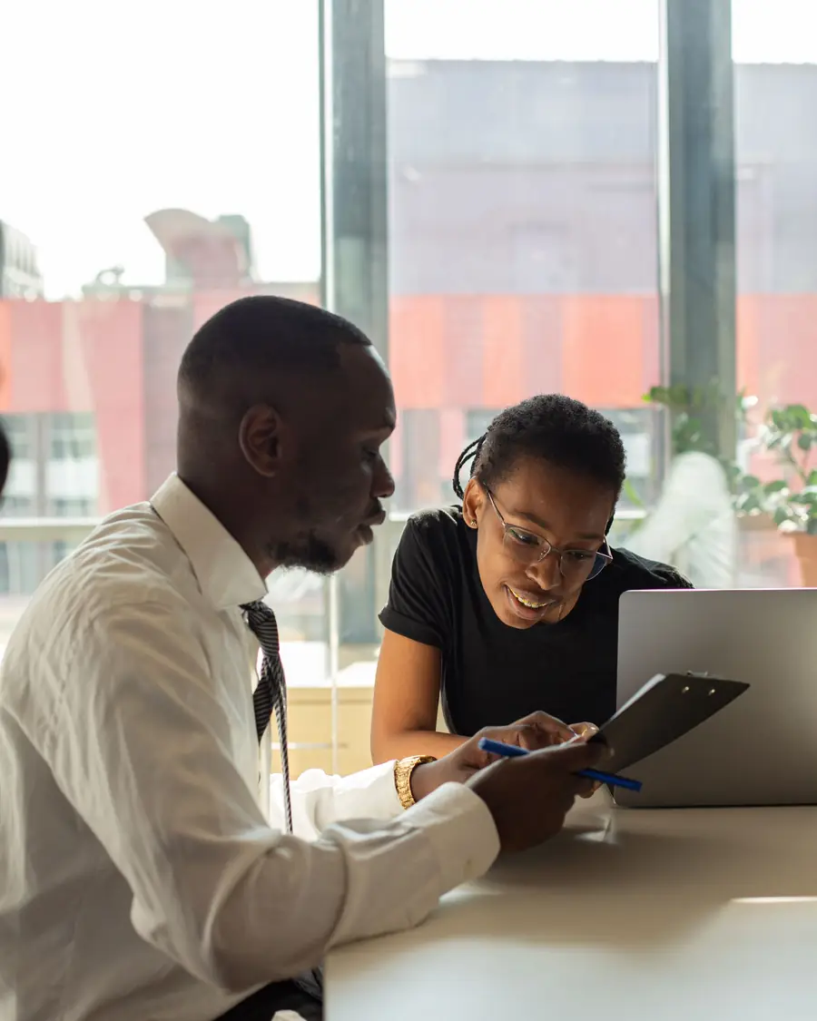 A mentor going through notes on a tablet with a young woman at a desk
