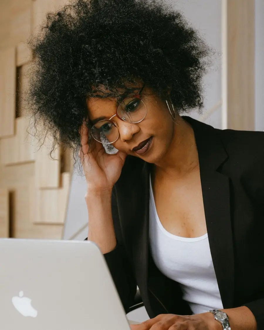 A young woman with her hand on her head, thinking hard in front of her laptop