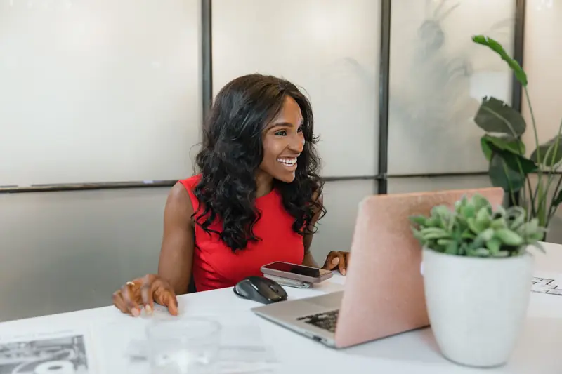 A young professional woman smiling at her laptop in a bright office
