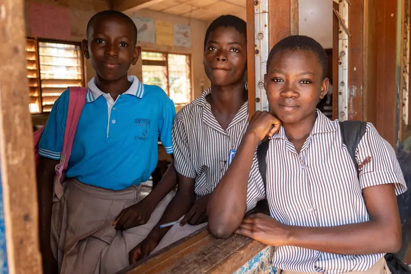 Three secondary-school students in uniform smiling in their classroom