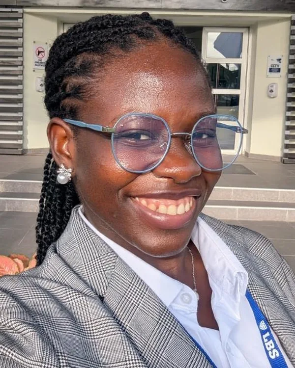Grace Eche smiling, wearing glasses and a grey checked blazer