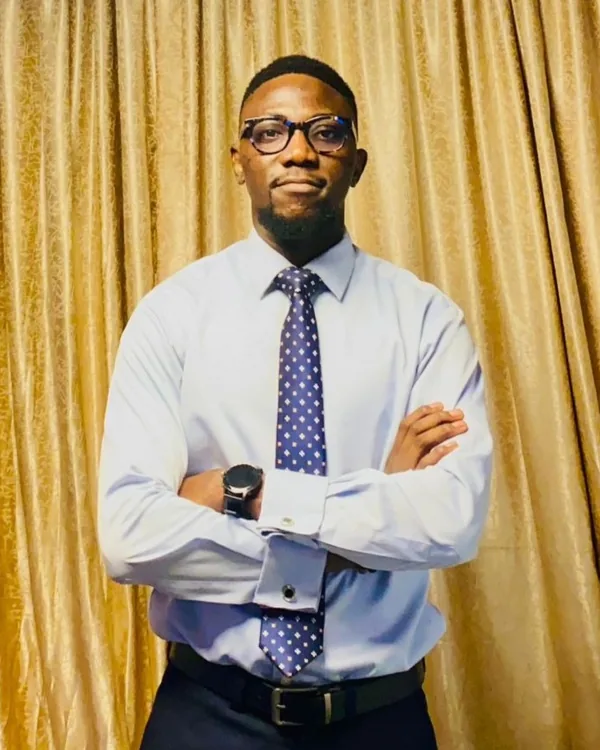 Damilare Olatoye smiling, wearing glasses and a burgundy suit, arms folded